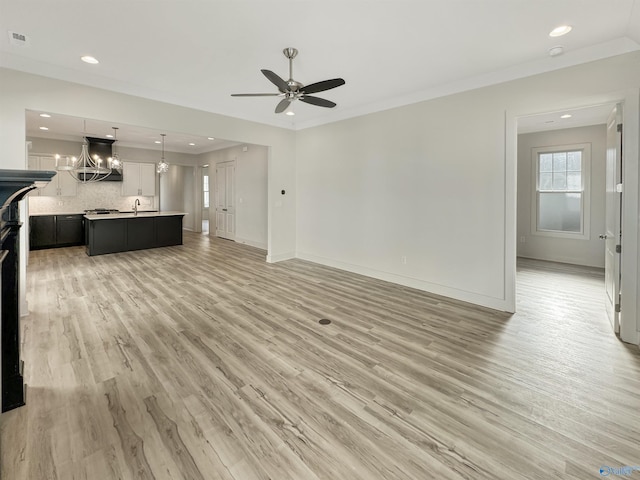 unfurnished living room featuring sink, ceiling fan with notable chandelier, ornamental molding, and light wood-type flooring