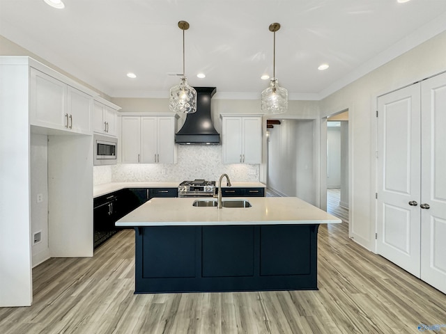 kitchen with sink, a kitchen island with sink, white cabinets, decorative light fixtures, and custom exhaust hood