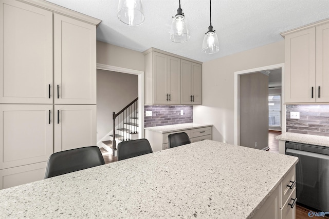 kitchen featuring light stone countertops, dishwasher, hanging light fixtures, a kitchen bar, and decorative backsplash