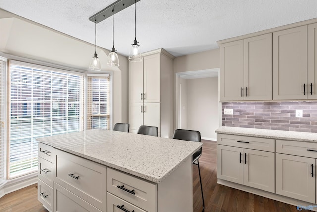 kitchen featuring a kitchen breakfast bar, hanging light fixtures, light stone countertops, dark wood-type flooring, and tasteful backsplash