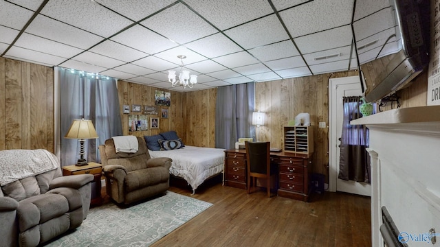 bedroom featuring wooden walls, a drop ceiling, a chandelier, and hardwood / wood-style flooring