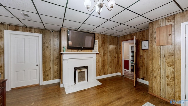 unfurnished living room with a chandelier, hardwood / wood-style floors, and wood walls