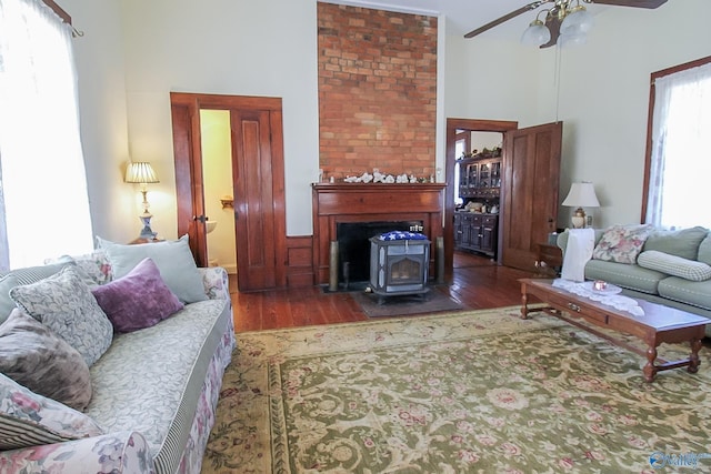 living room with dark hardwood / wood-style flooring, a wood stove, and ceiling fan