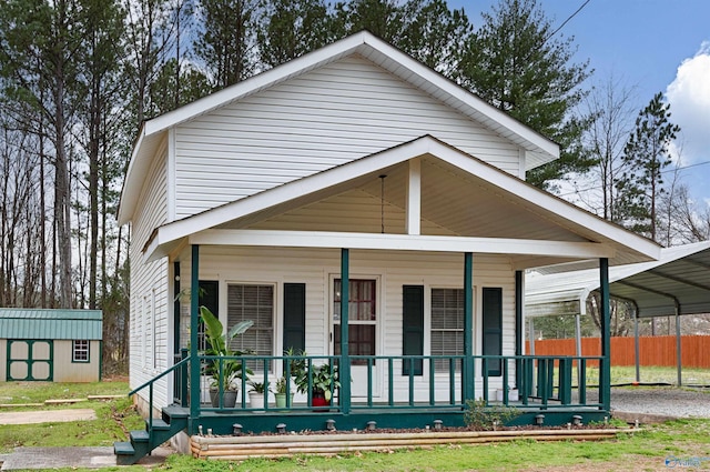 view of front of property featuring an outbuilding, a detached carport, fence, a porch, and a storage shed