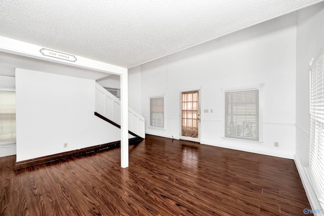 unfurnished living room with stairs, a textured ceiling, dark wood-type flooring, and baseboards