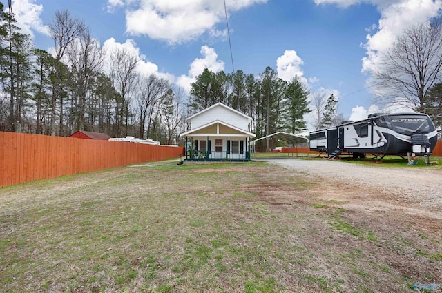 view of yard featuring a detached carport, a porch, fence, and dirt driveway