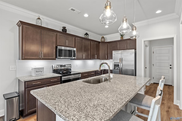 24009 Quints Dr, Athens, AL 35613 - kitchen featuring appliances with stainless steel finishes, a sink, dark brown cabinets, a breakfast bar area, and light stone countertops