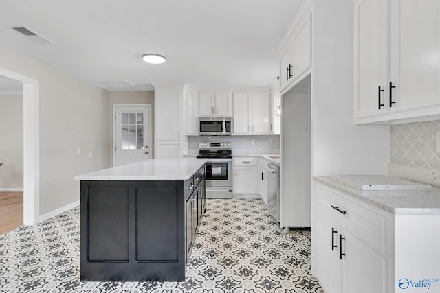 kitchen featuring appliances with stainless steel finishes, white cabinetry, tasteful backsplash, light stone countertops, and a kitchen island