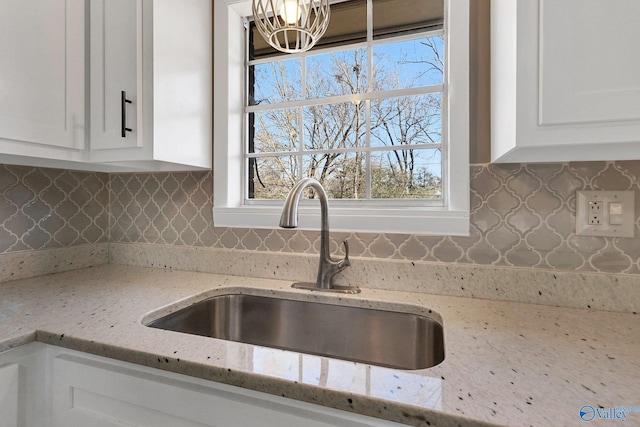 kitchen with white cabinetry, sink, backsplash, and light stone countertops