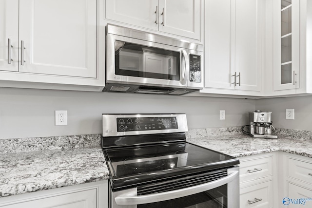 kitchen with appliances with stainless steel finishes, white cabinets, and glass insert cabinets