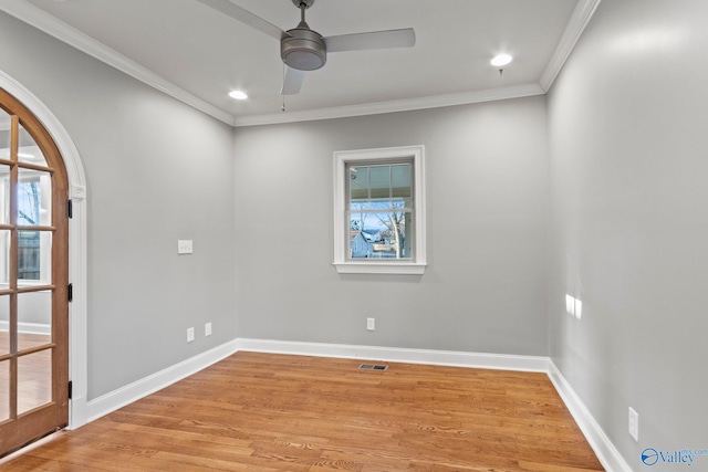 spare room featuring light wood-style floors, baseboards, arched walkways, and ornamental molding