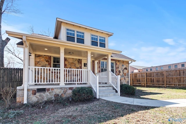 view of front of property with stone siding, fence, and a porch