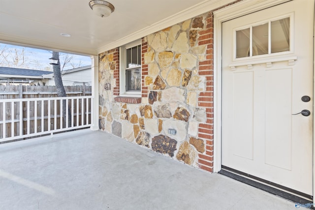 entrance to property featuring stone siding, covered porch, brick siding, and fence