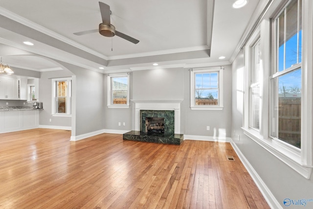 unfurnished living room with crown molding, a raised ceiling, light wood-style flooring, a high end fireplace, and baseboards