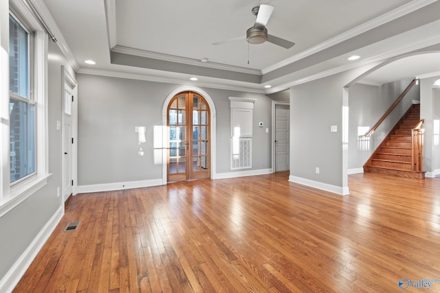 unfurnished living room featuring light wood-type flooring, arched walkways, a raised ceiling, and visible vents