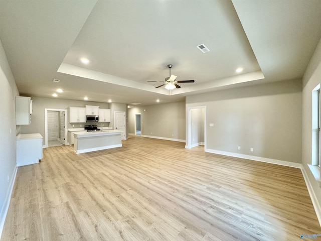 unfurnished living room with ceiling fan, a raised ceiling, and light hardwood / wood-style flooring