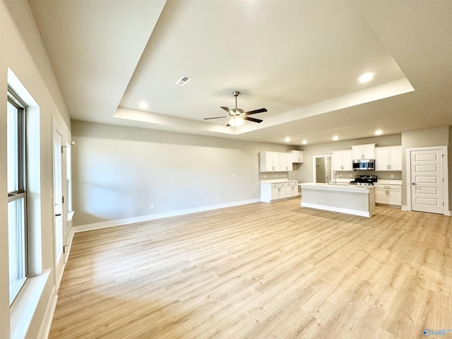 unfurnished living room featuring ceiling fan, a tray ceiling, light hardwood / wood-style floors, and a wealth of natural light