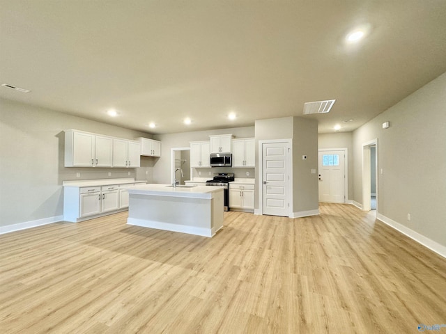 kitchen with sink, stainless steel appliances, an island with sink, white cabinets, and light wood-type flooring