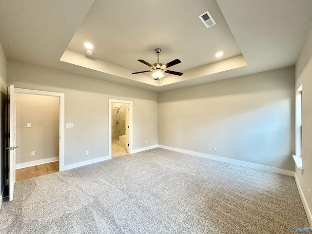 unfurnished bedroom featuring a raised ceiling, ensuite bathroom, carpet flooring, and ceiling fan