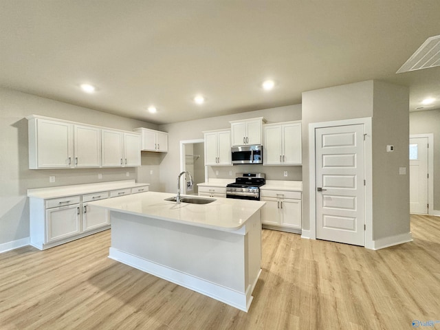 kitchen with sink, stainless steel appliances, white cabinets, a center island with sink, and light wood-type flooring