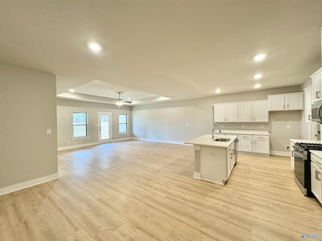 kitchen featuring a raised ceiling, white cabinetry, a kitchen island with sink, stainless steel appliances, and light wood-type flooring