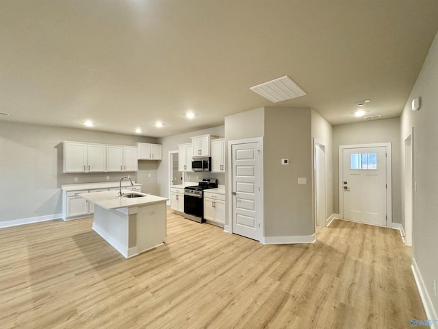 kitchen with sink, white cabinetry, stainless steel appliances, light hardwood / wood-style floors, and a center island with sink