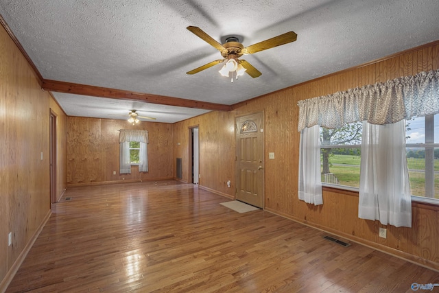 spare room featuring a textured ceiling, visible vents, a ceiling fan, hardwood / wood-style floors, and wooden walls