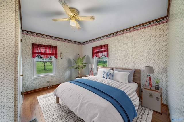 bedroom featuring hardwood / wood-style flooring, a ceiling fan, multiple windows, and wallpapered walls