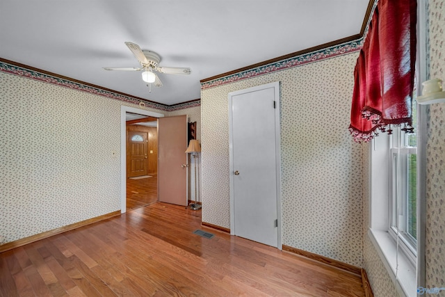 spare room with visible vents, wallpapered walls, a ceiling fan, wood finished floors, and crown molding