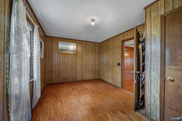 unfurnished room with wooden walls, baseboards, wood finished floors, and a textured ceiling