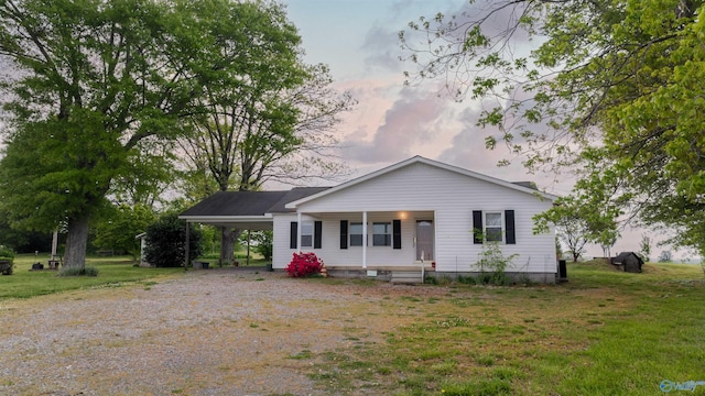 view of front of house with a porch, gravel driveway, an attached carport, and a yard
