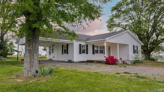 view of front of house with a yard, dirt driveway, a carport, and covered porch