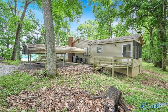 rear view of property with a carport, a sunroom, and a chimney