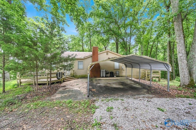 view of side of home with a carport, driveway, a wooden deck, and a chimney