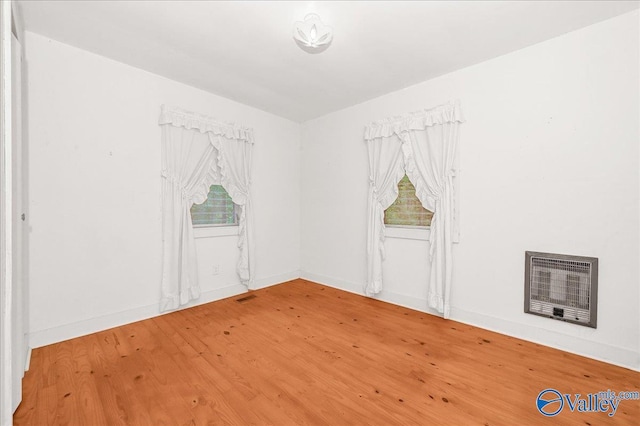 unfurnished room featuring baseboards, heating unit, a healthy amount of sunlight, and wood finished floors