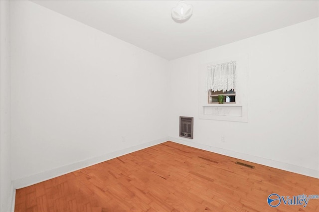 spare room featuring heating unit, wood finished floors, visible vents, and baseboards