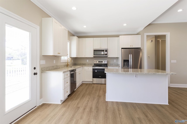 kitchen with light wood finished floors, a kitchen island, a sink, stainless steel appliances, and crown molding