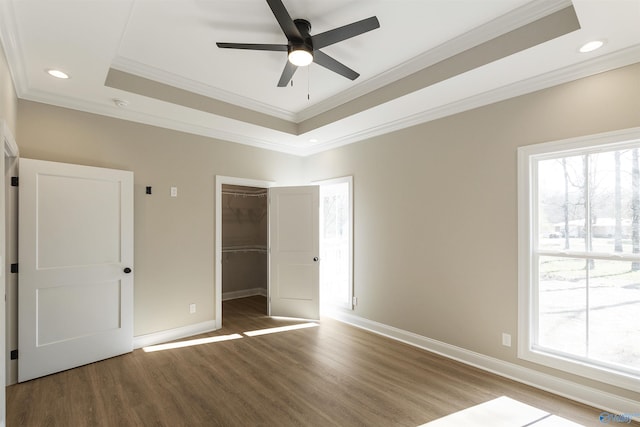 unfurnished bedroom featuring a tray ceiling, multiple windows, baseboards, and wood finished floors