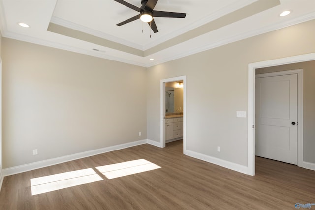 unfurnished bedroom featuring baseboards, crown molding, a tray ceiling, and wood finished floors