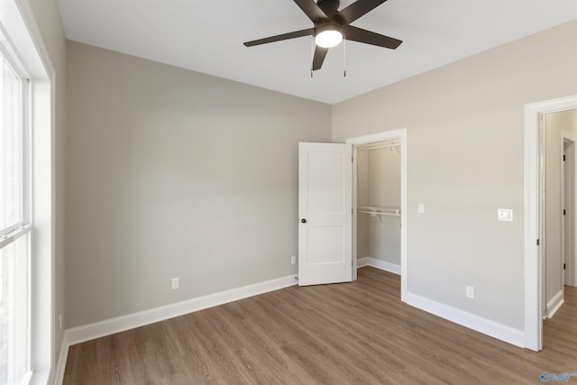 unfurnished bedroom with a walk in closet, ceiling fan, baseboards, wood finished floors, and a closet