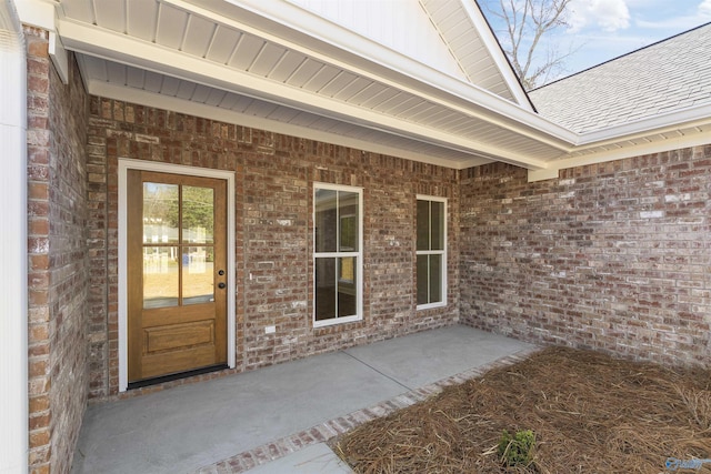 view of exterior entry with board and batten siding, brick siding, and a shingled roof