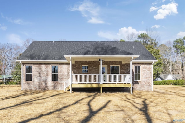 back of property featuring brick siding, covered porch, and roof with shingles