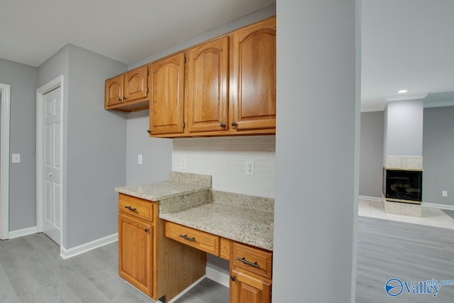 kitchen with light wood finished floors, light stone counters, baseboards, and decorative backsplash