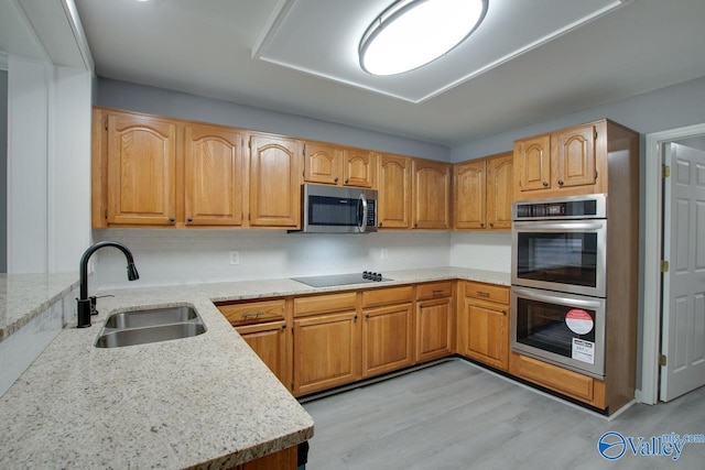 kitchen with light stone countertops, stainless steel appliances, a sink, decorative backsplash, and light wood finished floors