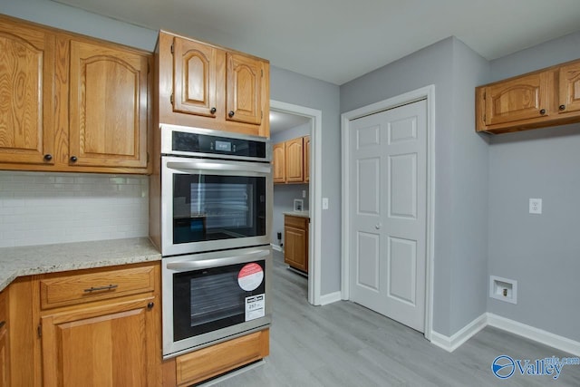 kitchen featuring stainless steel double oven, baseboards, decorative backsplash, light stone countertops, and light wood finished floors