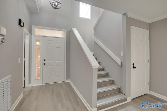 foyer featuring light wood finished floors, baseboards, stairway, and visible vents