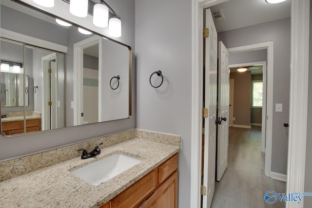 bathroom with visible vents, vanity, baseboards, and wood finished floors