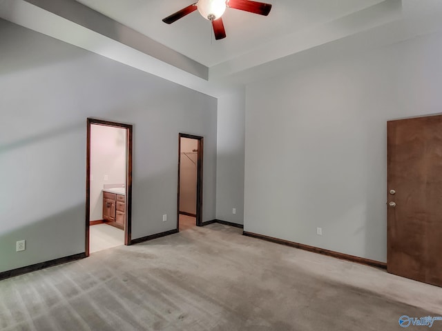 unfurnished bedroom with a walk in closet, light colored carpet, connected bathroom, and ceiling fan