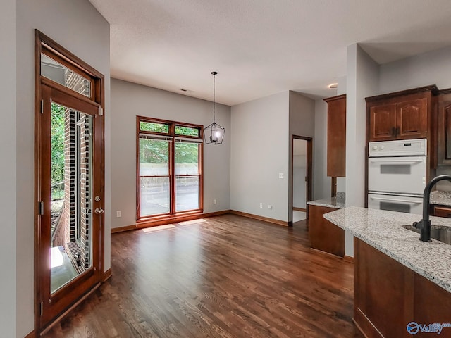 kitchen featuring sink, dark wood-type flooring, white double oven, light stone counters, and decorative light fixtures