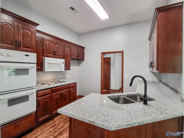 kitchen with sink, light stone counters, white appliances, and light hardwood / wood-style flooring